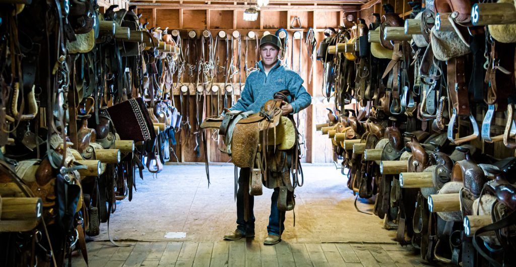 Wrangler holding saddle in tackroom at Greenhorn Ranch
