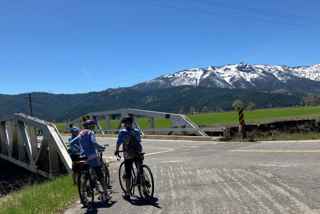 Two cyclists just before bridge near Taylorsville with snow capped mountain in distance