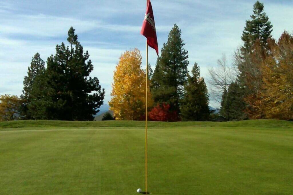 Golf hole with flag in and trees with fall color in background