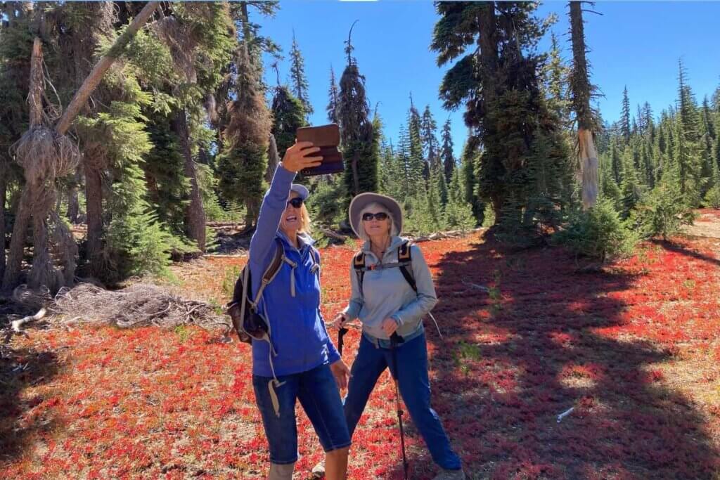 Two women with selfie on PCT Lakes Basin above Silver Lake with a carpe of red fall colors